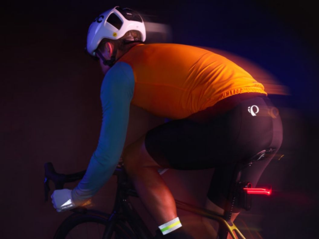 A rider in the dark wearing reflective and high-vis riding apparel pedals. Their tail light casts a small light streak behind. 